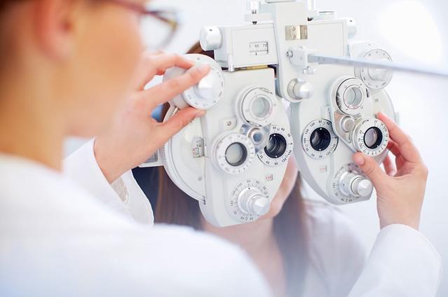 سيدة شابة خلف جهاز فحص العين بينما يفحص طبيب العيون عينيها خلال إجراء فحص العين.